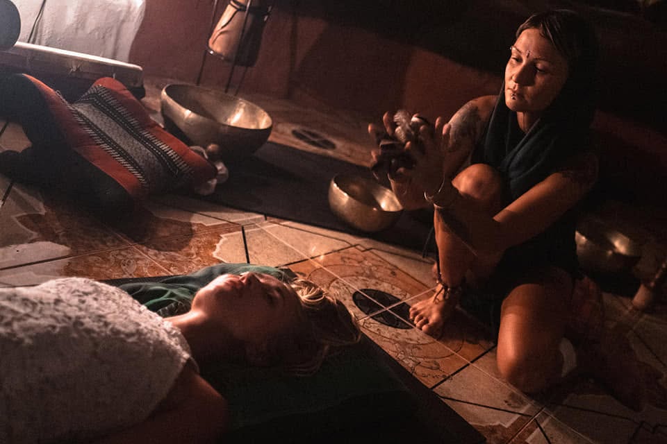 Anna working with sound over a participant, surrounded by singing bowls
