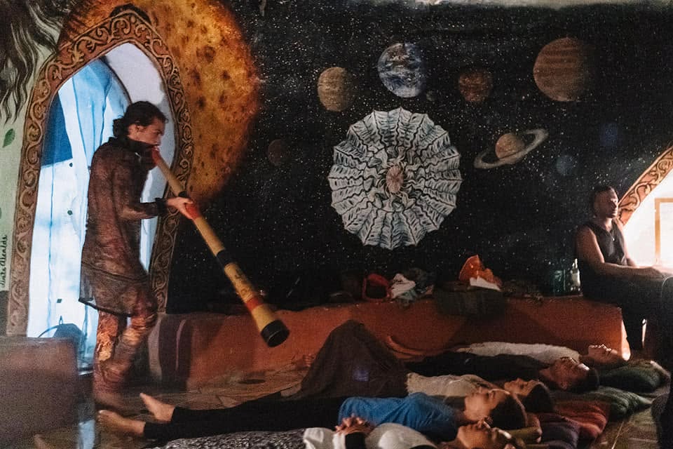 Oliv playing didgeridoo over a group lying in a temple space
